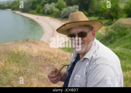 Outdoor portrait of happy senior man in dark sunglasses and straw hat Stock Photo