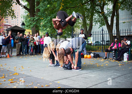 NEW YORK CITY - OCTOBER 18, 2014: a man from a perfomance group is doing a somersault over a line of tourists on the street in Lower Manhattan Stock Photo