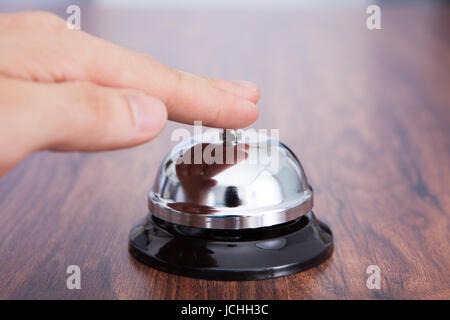 Close-up Of Hand Ringing Service Bell Kept On Wooden Table Stock Photo