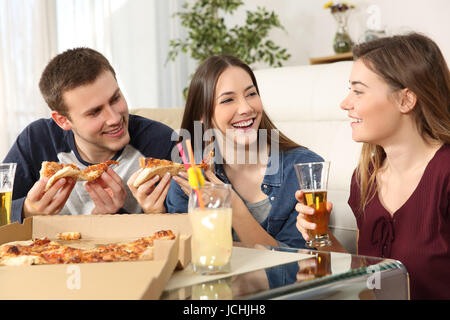 Three friends talking and eating pizza sitting on the floor in the living room at home Stock Photo