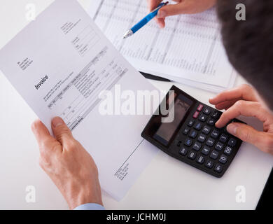 Over the shoulder view of a man checking an invoice on a calculator Stock Photo