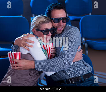 Couple sitting in seats at a cinema wearing 3D glasses reacting to the reality of the dimensional image in a scene in the movie Stock Photo