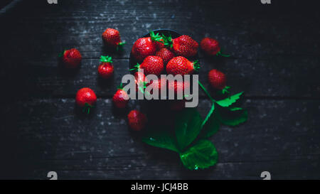 Strawberry in a bowl with leaves on an old wooden board Stock Photo