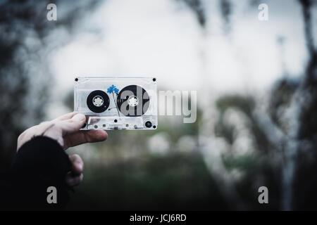 A man holds in his hand an old cassette tape with a flower inside against the sky and trees. Concept: nostalgic time. Stock Photo
