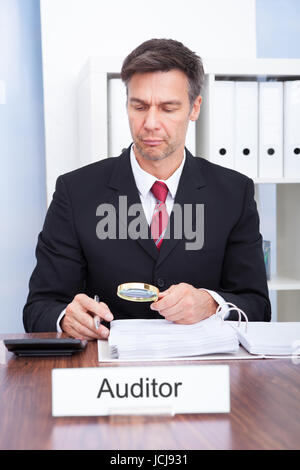 Businessman Looking At Document Through Magnifying Glass Stock Photo
