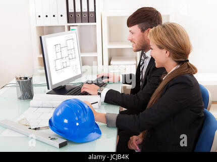 Two professional architects or structural engineers sitting at a desk looking at a computer discussing a building plan Stock Photo