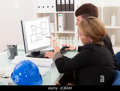 Two professional architects or structural engineers sitting at a desk looking at a computer discussing a building plan Stock Photo