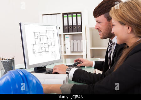Two professional architects or structural engineers sitting at a desk looking at a computer discussing a building plan Stock Photo