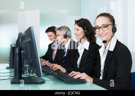 Line of professional stylish call centre operators wearing headsets seated behind their computers giving assistance Stock Photo