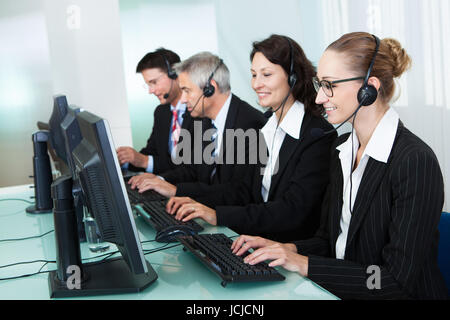 Line of professional stylish call centre operators wearing headsets seated behind their computers giving assistance Stock Photo