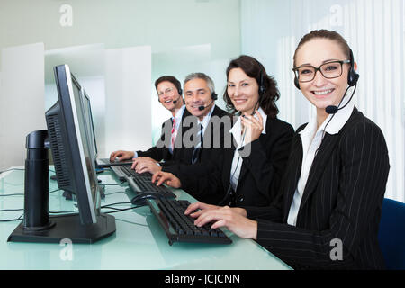 Line of professional stylish call centre operators wearing headsets seated behind their computers giving assistance Stock Photo