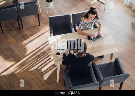 Two women are sitting at the table and discussing job problems and solving issues in work. Stock Photo