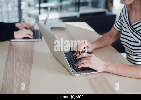 Close up picture of hands of two businesswomen typing on their tablet computer and laptop. Stock Photo