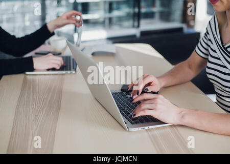 Close up shot of female workers in office writing information. Two ladies are sitting at a table and typing on laptops. Stock Photo