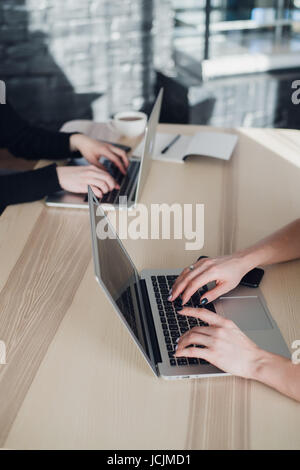 Two ladies are sitting at a table and typing on laptops. Close up shot of female workers in office doing job. Stock Photo
