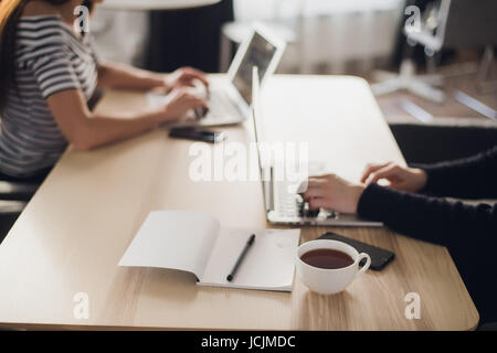 Place of work. Close-up shot of comfortable working place in office with wooden table and laptop coffee of cup smart phone notepad and mouse laying on it. Stock Photo