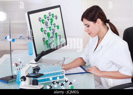 Female Scientist Sitting In Laboratory And Writing On Clipboard Stock Photo
