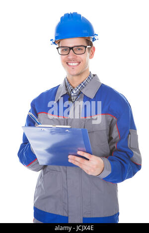 Young Construction Reviewer Wearing Workwear And Hardhat Writing On Clipboard Stock Photo