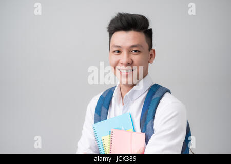 Happy casual asian male student holding books isolated on a gray background Stock Photo