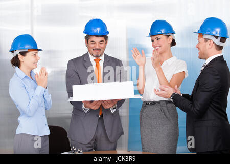 Happy Coworkers Applauding For A Architect Holding Architectural Model Stock Photo