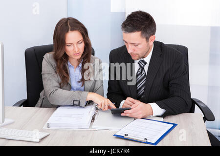 Two Young Businesspeople Calculating Bills At Desk In Office Stock Photo