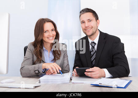 Two Young Businesspeople Calculating Bills At Desk In Office Stock Photo