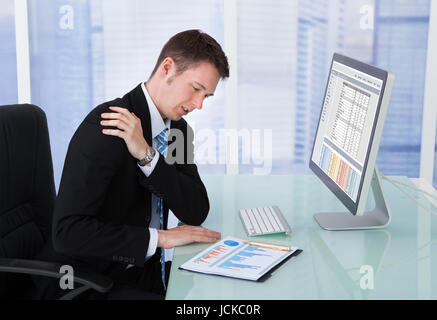 Young businessman having shoulder pain while working at computer desk in office Stock Photo