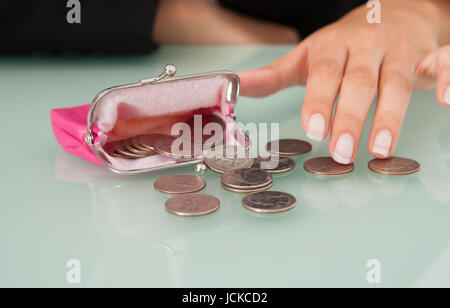 Midsection of businesswoman counting coins spilled from pink purse at office desk Stock Photo