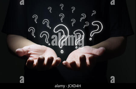 Businessman holding drawn question marks in his hand with dark background , Business question concept . Stock Photo