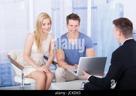 Financial advisor explaining investment plan to young couple on laptop in office Stock Photo
