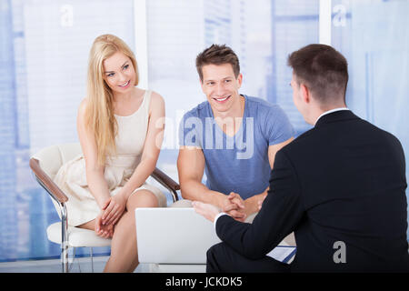 Financial advisor explaining investment plan to young couple on laptop in office Stock Photo