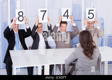 Business people showing score cards in front of female candidate during interview Stock Photo