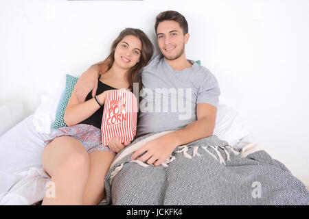 Young couple watching movies in bed and eating popcorn. Indoors. Stock Photo