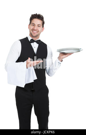 Portrait of confident young waiter with napkin and serving tray standing isolated over white background Stock Photo