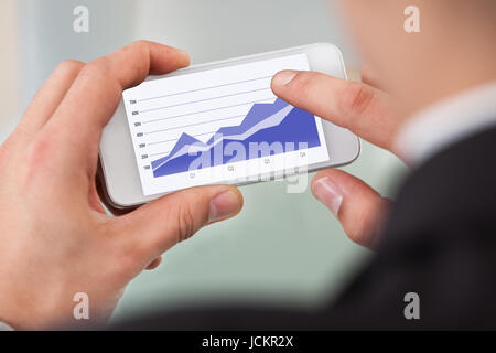 Cropped image of businessman analyzing graph on smart phone in office Stock Photo