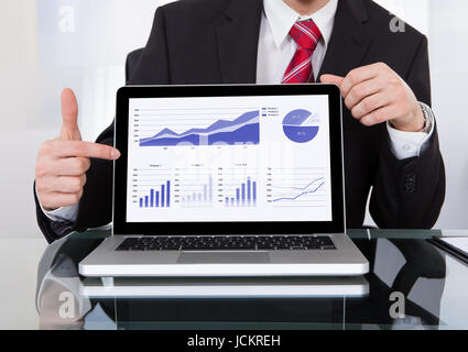 Portrait of confident businessman displaying laptop at desk in office Stock Photo