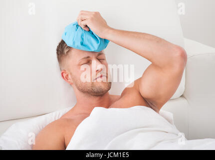 Man nursing a hangover after a heavy night of partying holding an ice pack to his forehead with his eyes closed on pain against the throbbing Stock Photo