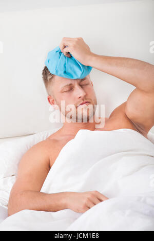 Man nursing a hangover after a heavy night of partying holding an ice pack to his forehead with his eyes closed on pain against the throbbing Stock Photo