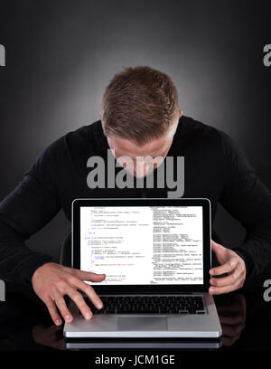 Man or hacker stealing data from a laptop at night bending forwards over the keyboard in the glow from the screen as he browses the internet or retrieves and downloads personal data Stock Photo