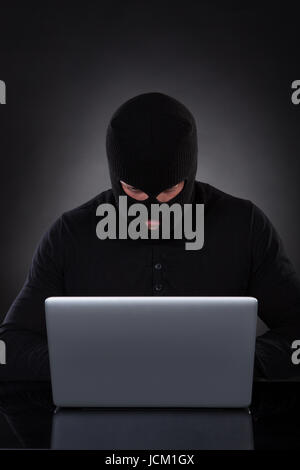 Man or hacker working on a laptop computer at night bending forwards over the keyboard in the glow from the screen as he browses the internet or retrieves and downloads personal data Stock Photo