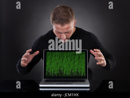 Man or hacker stealing data from a laptop at night bending forwards over the keyboard in the glow from the screen as he browses the internet or retrieves and downloads personal data Stock Photo