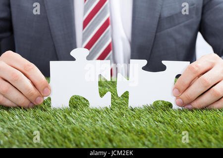 Closeup of businessman joining puzzle pieces on grass Stock Photo