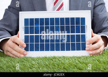 Midsection of businessman holding solar panel on meadow Stock Photo