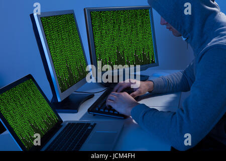 High angle view of hacker in hooded jacket using computer at table Stock Photo
