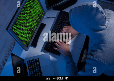 High angle view of hacker in hooded jacket using computer at table Stock Photo