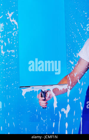 Cropped image male servant cleaning glass with squeegee over blue background Stock Photo