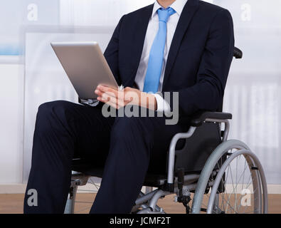 Close-up image of disabled businessman using digital tablet on wheelchair in office Stock Photo