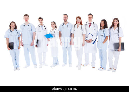 Large diverse group of doctors and nurses in uniform standing in a line holding files of patient records and wearing stethoscopes  isolated on white Stock Photo