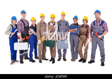 Large group of diverse workmen and women standing in a row holding their tools and equipment and wearing hardhats  isolated on white Stock Photo