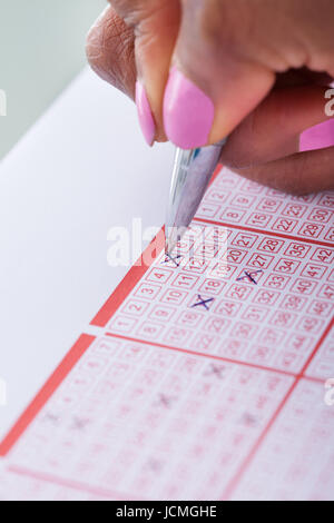 Cropped image of woman's hand marking numbers on lottery ticket with pen at table Stock Photo
